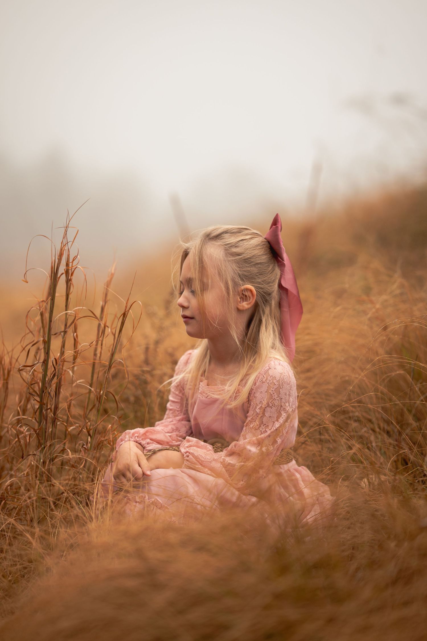 A dreamy portrait of someone wearing a pink dress sitting in golden autumn grass at sunset.