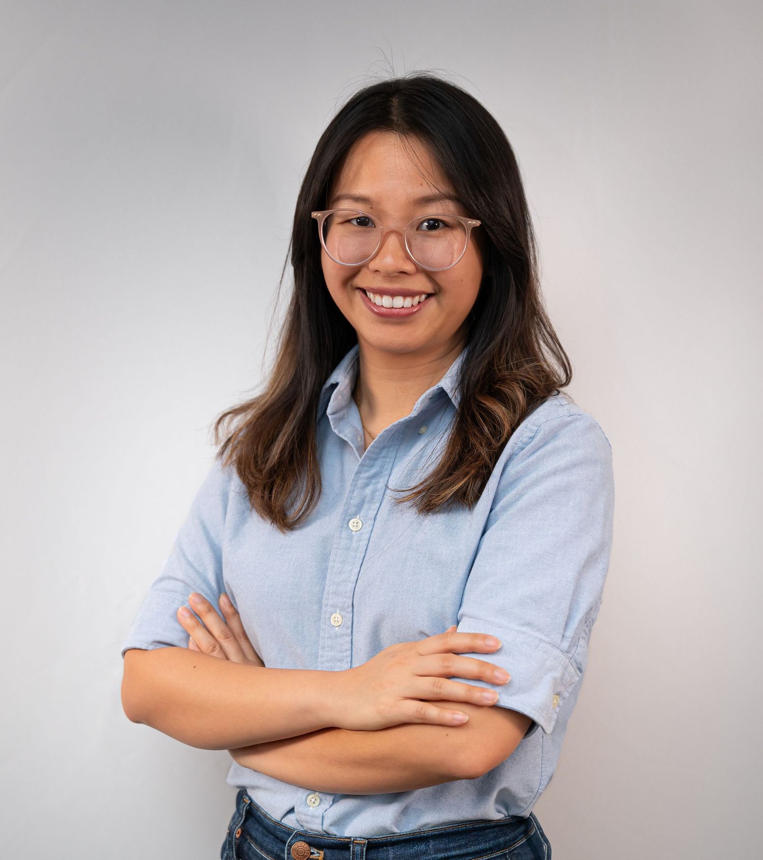 Professional headshot portrait of someone wearing a light blue button-down shirt against a neutral gray background.