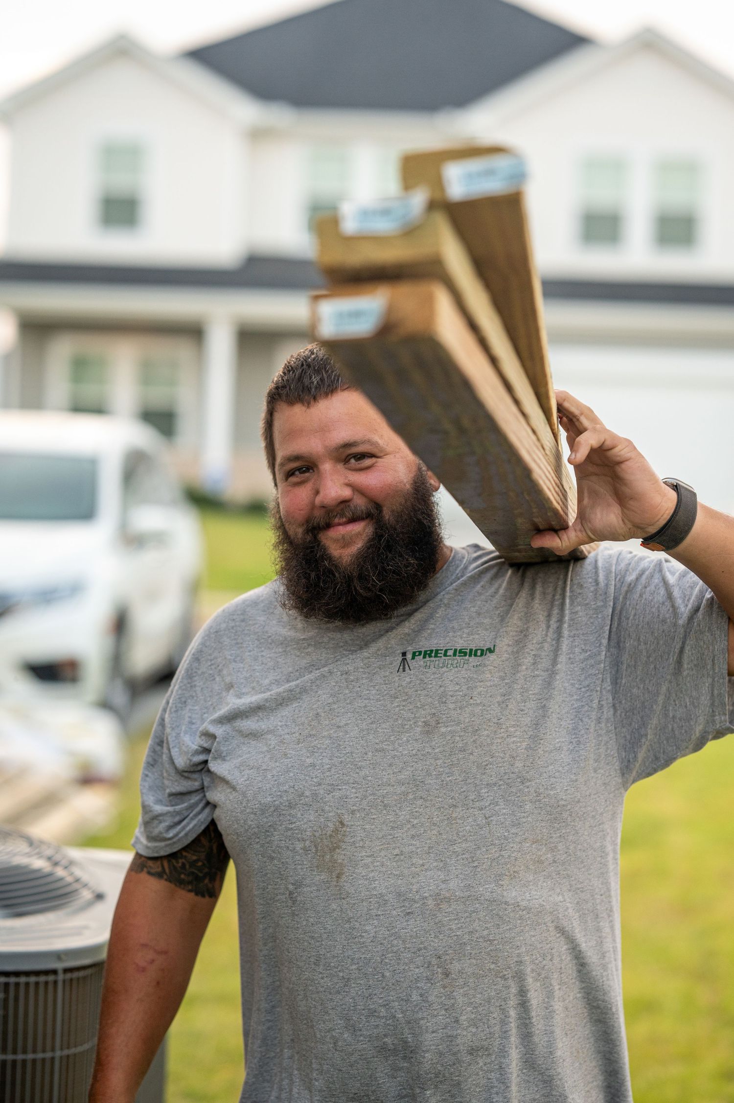 Person in grey shirt carrying lumber materials outside residential home.
