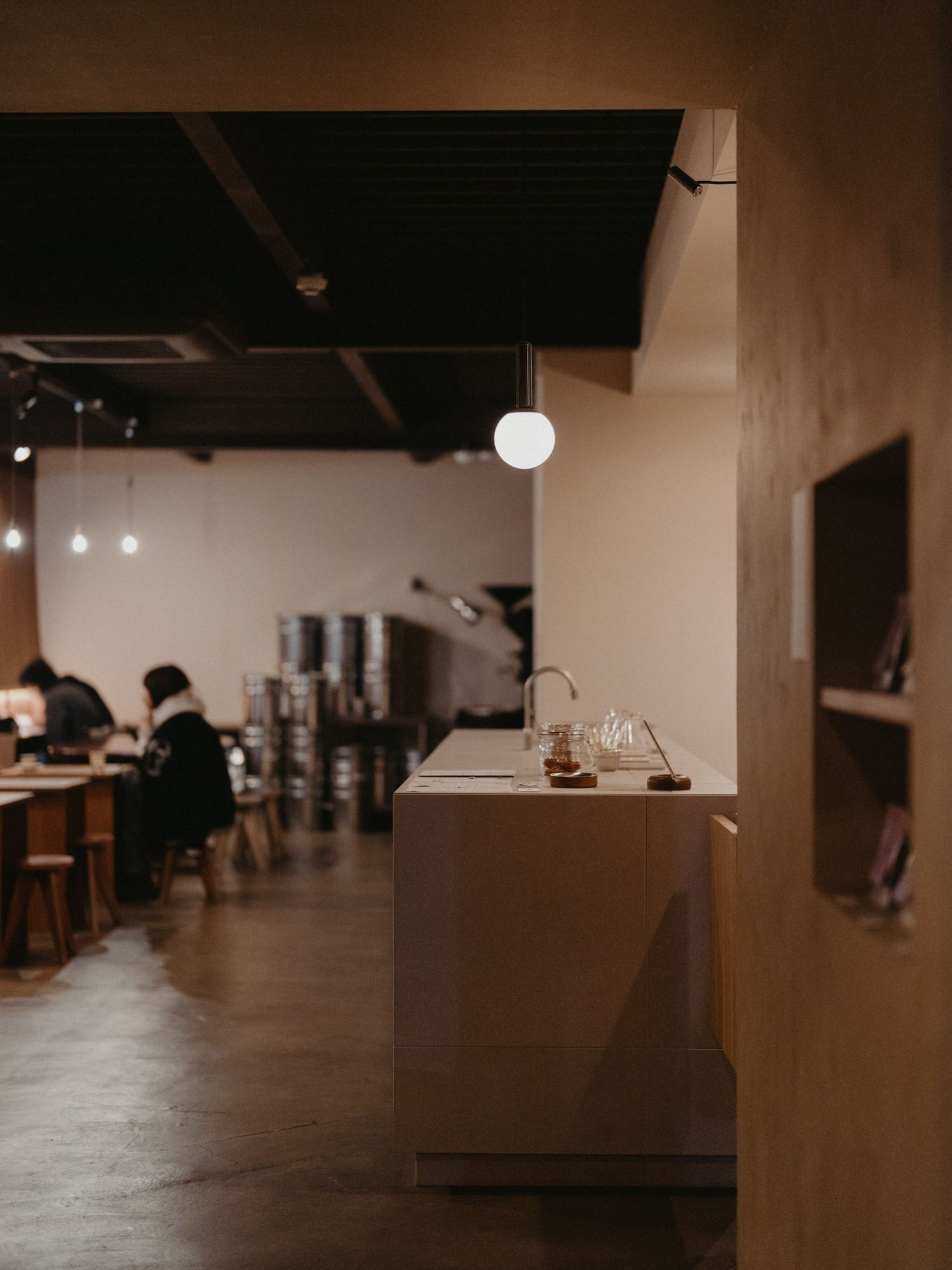 Modern coffee shop interior with wooden counter, pendant lighting and minimalist decor in warm moody tones.