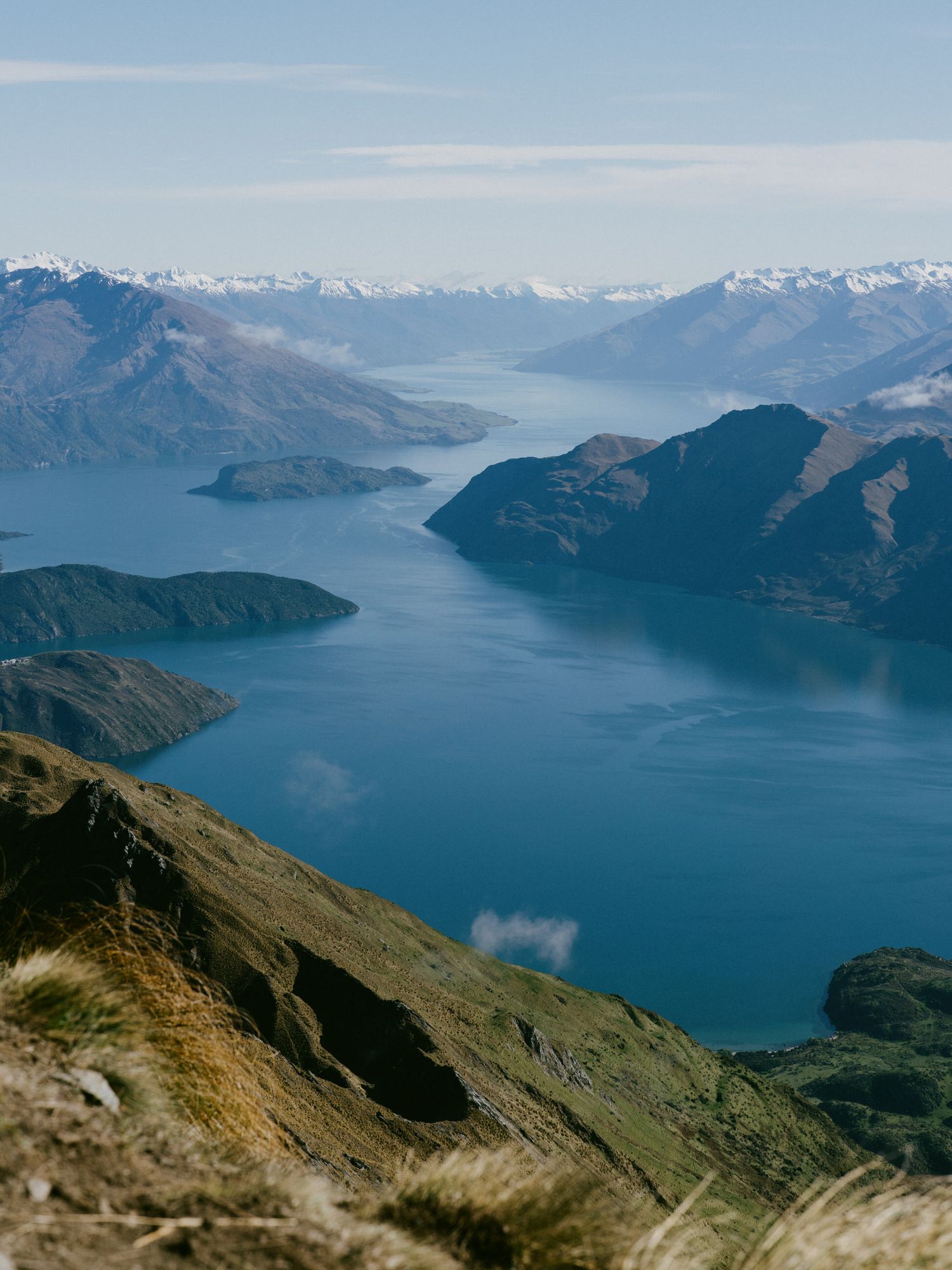 Panoramic view of Lake Wanaka in New Zealand with snow-capped mountains and blue waters stretching to the horizon.