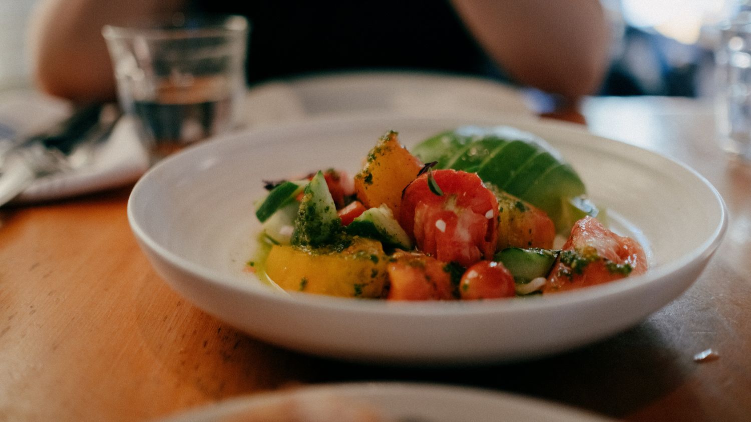 Fresh heirloom tomato salad with avocado and herbs served in a white bowl at a restaurant.