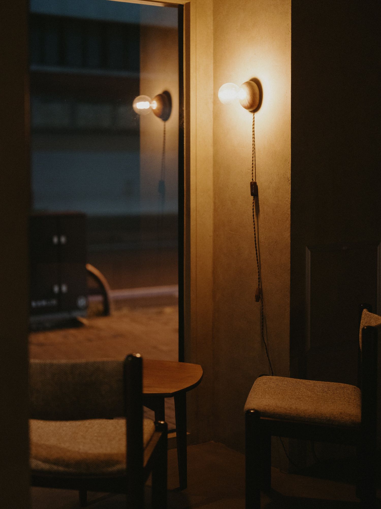 A dimly lit interior room with warm wall sconces and wooden furniture creating a cozy, intimate atmosphere.