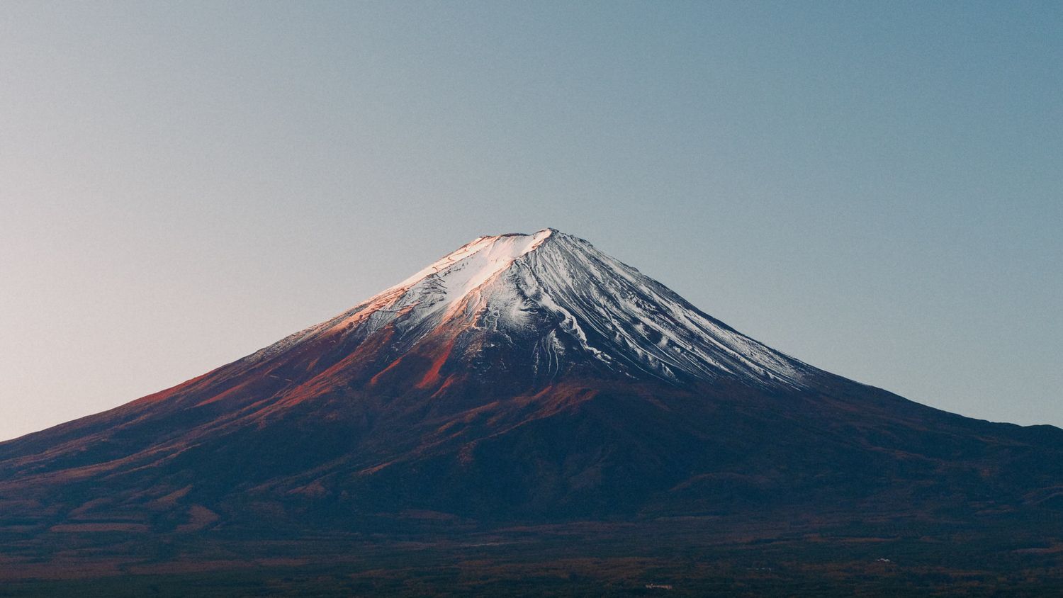 Snow-capped Mount Fuji stands majestically against a clear blue sky in Japan.