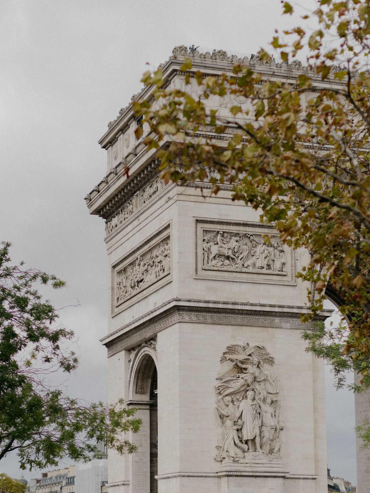 Multiple views of the historic Arc de Triomphe monument in Paris framed by autumn tree branches against a cloudy sky.