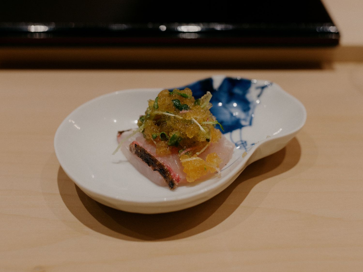 A series of small plates with elegant Japanese sashimi and sushi dishes arranged on a wooden counter.