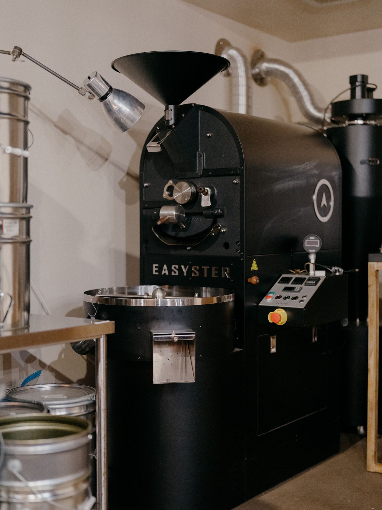 Professional coffee roasting equipment with black and silver machines in a commercial kitchen setting.