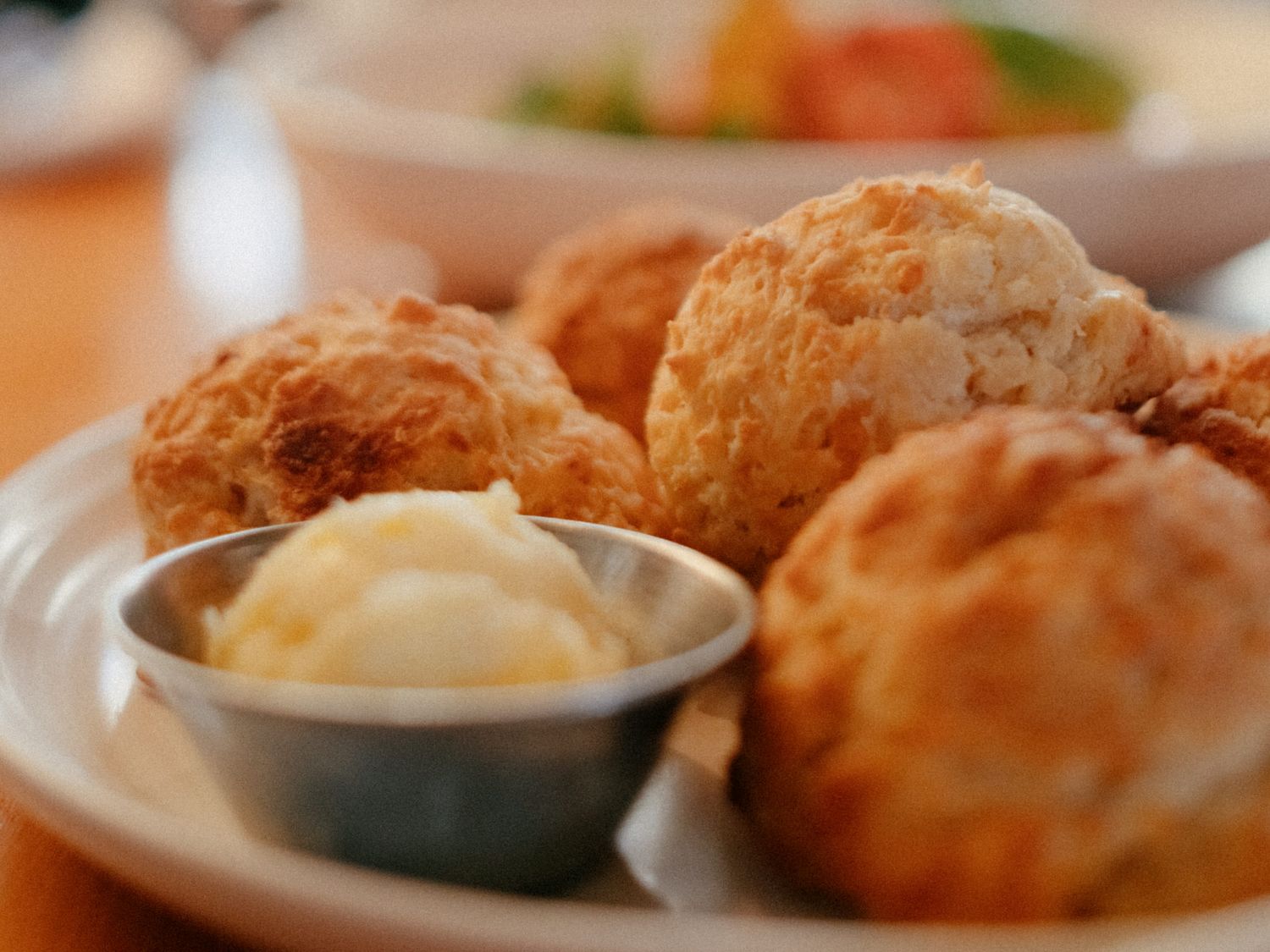 Freshly baked golden biscuits served on a white plate with a small bowl of creamy butter.
