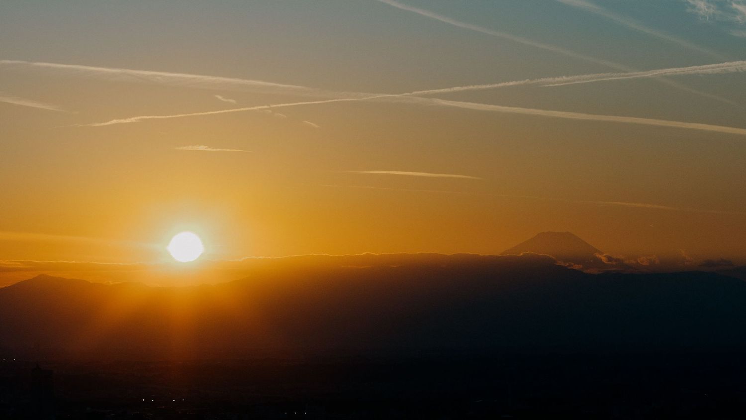 A stunning orange and pink sunset illuminates the silhouette of mountain landscapes against the darkening horizon.