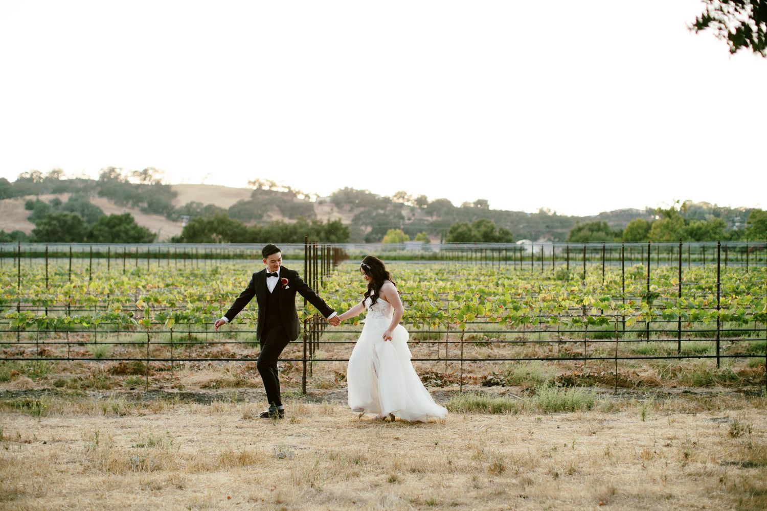 Couple running together through a vineyard on a sunny afternoon.