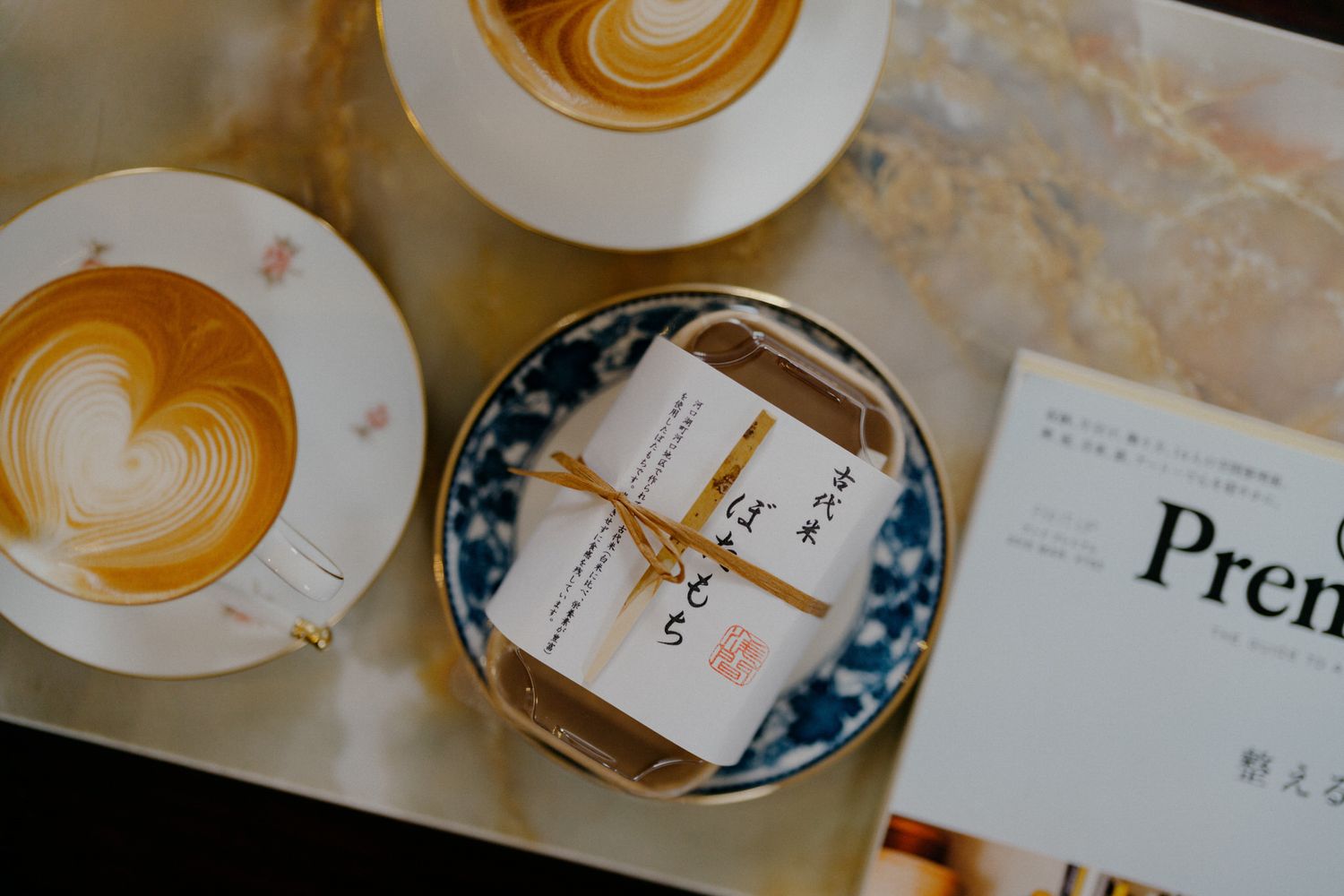 Multiple latte art hearts and rosettes in white ceramic cups arranged on a wooden table with Japanese style patterns.