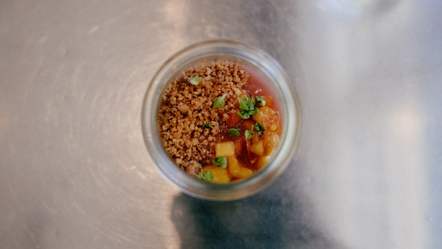 Overhead view of a gourmet small dish with crispy grains, fresh vegetables, and colorful garnishes in a glass bowl.