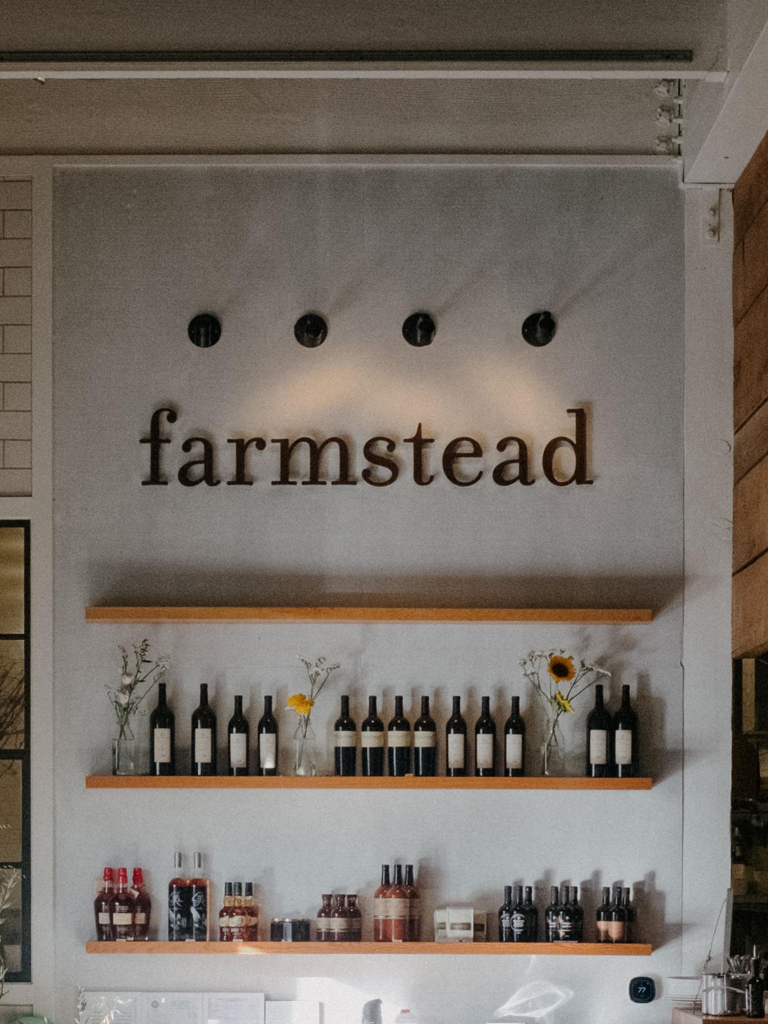 Farmstead restaurant wall display with wine bottles on wooden shelves and branded signage with accent lights.