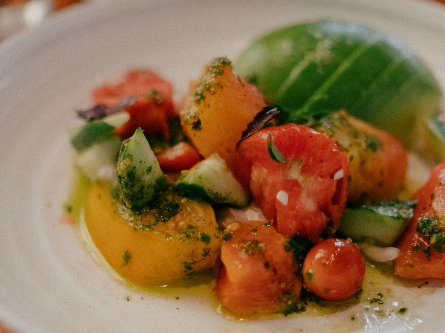 Fresh heirloom tomato salad with cucumber, herbs, and olive oil dressing served on a white plate.