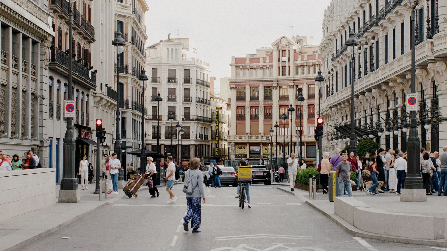 Pedestrians walk through a bustling street in Madrid's city center lined with historic buildings and modern shops.