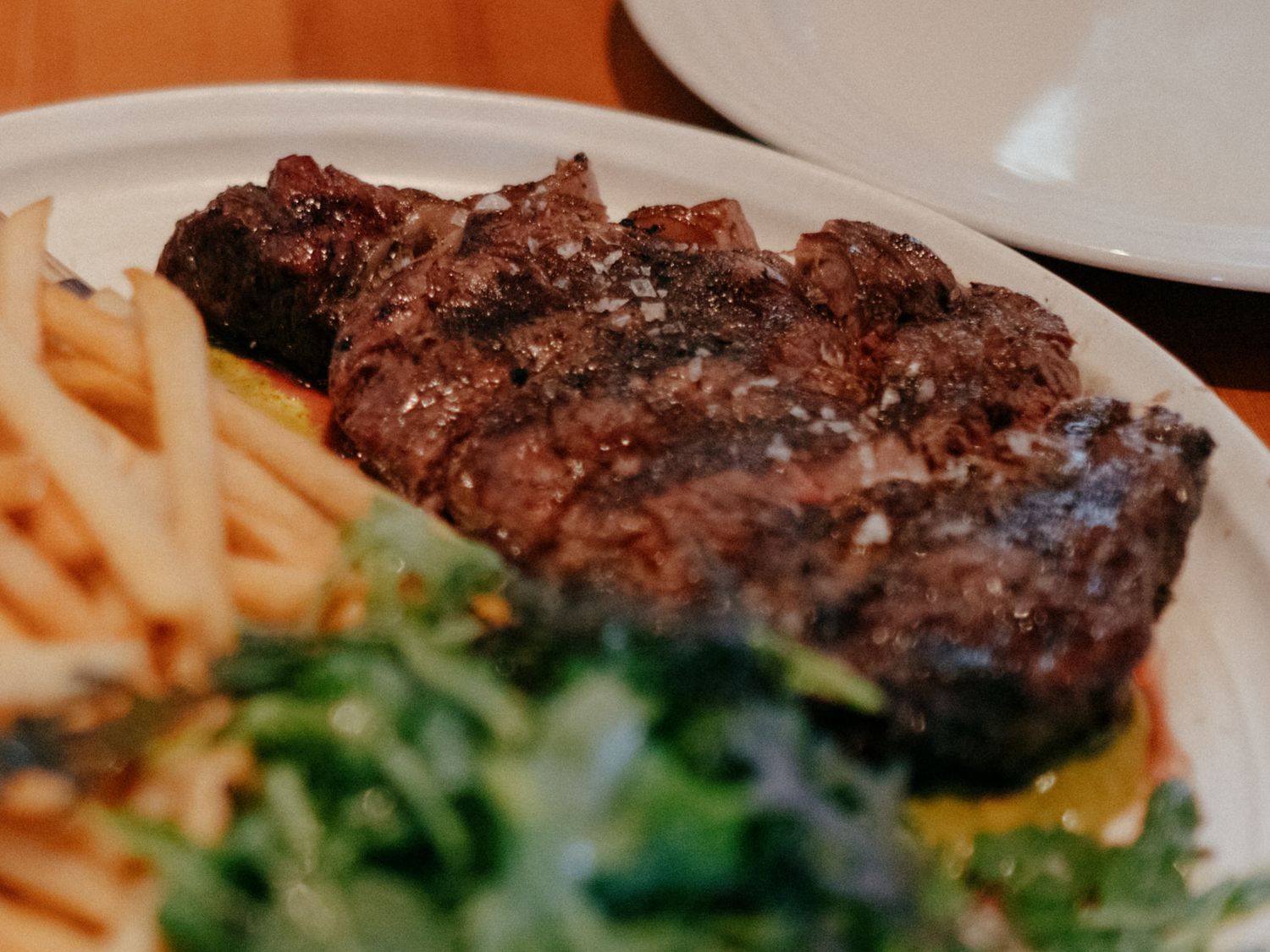Grilled steak served with crispy french fries and fresh green salad on a white plate.