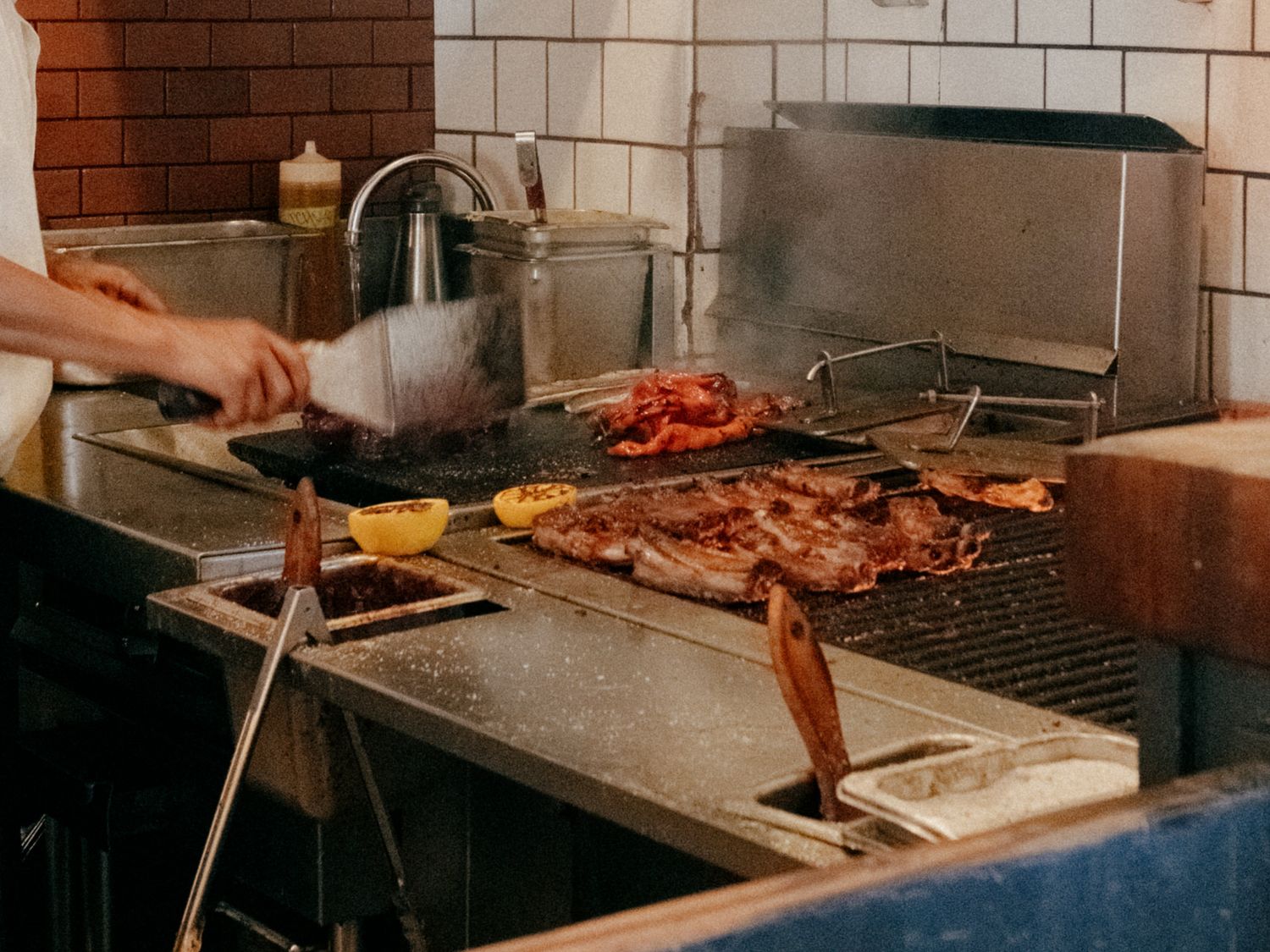 Chef grilling assorted meats including ribs and lobster on a commercial kitchen grill.
