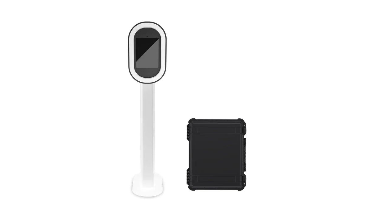 White freestanding photo booth kiosk with circular light ring display and black protective carrying case.