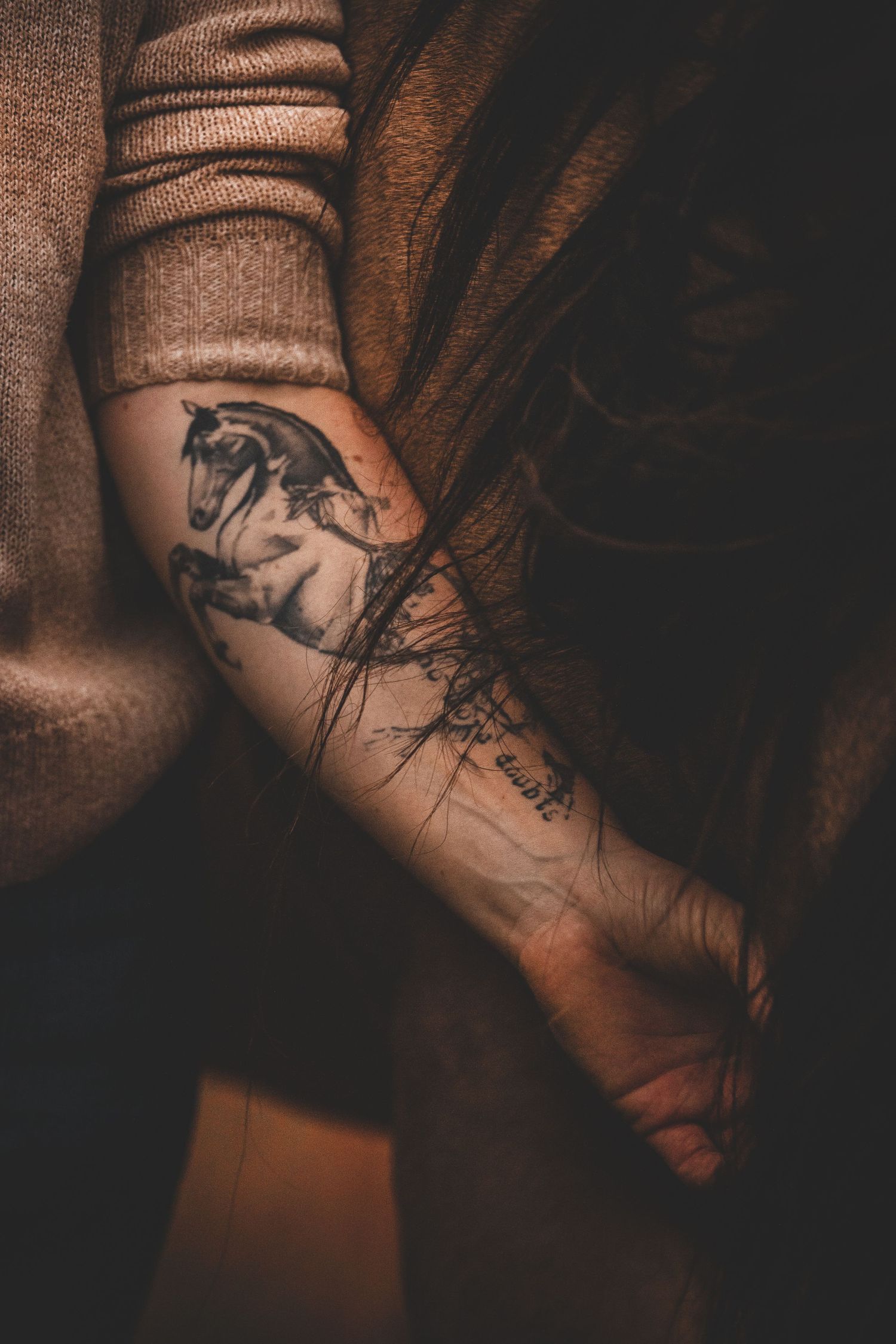 Frau hält Arm mit einem Pferde-Tattoo an die Mähne ihres Pferdes und baut eine innige Verbindung auf
