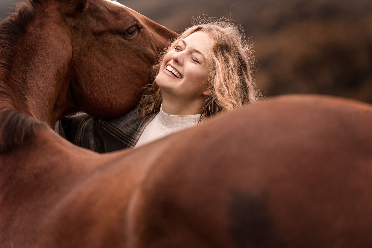 Blonde junge Frau wird von fuchsfarbenem Pferd beim Fotoshooting eingerahmt