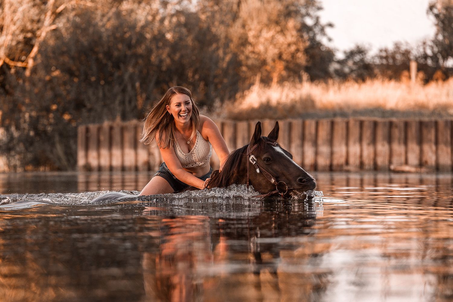 Blonde Frau schwimmt mit ihrem schwarzen Pferd im Wasser