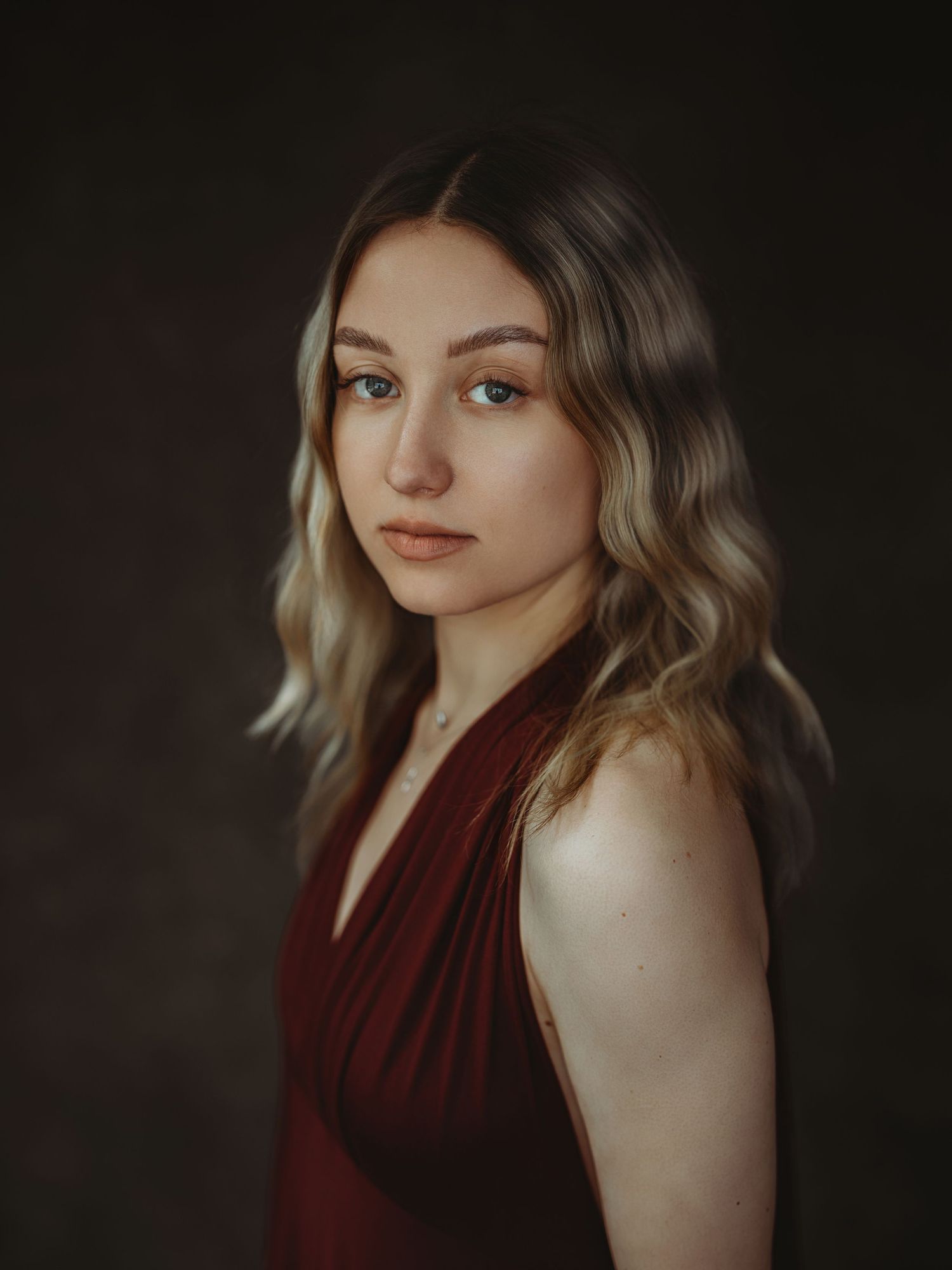 Portrait series in burgundy dress against dark background showcasing dramatic lighting and contemplative poses.