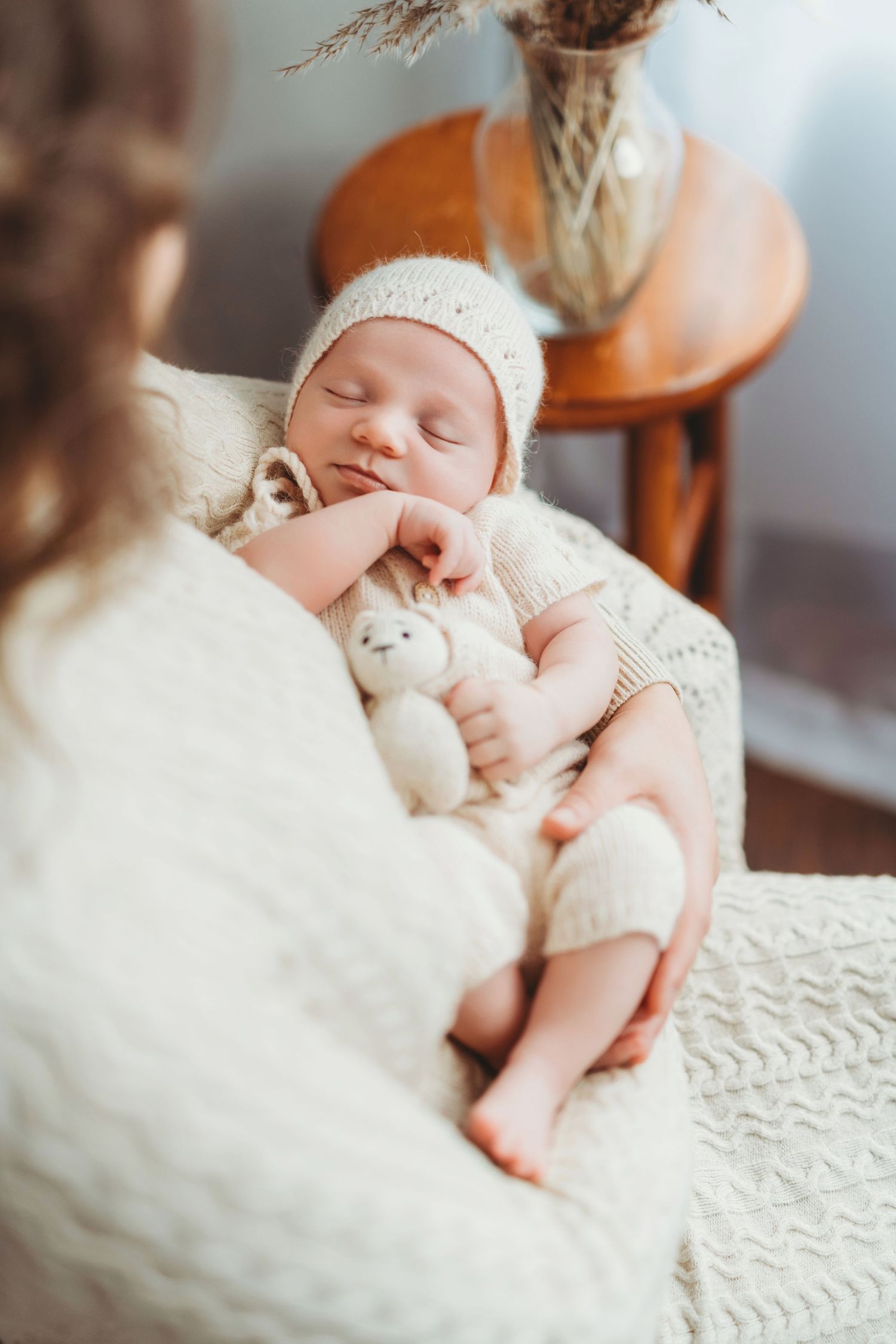 A sleeping newborn in a white knit outfit cuddles with a small plush toy while resting in soft blankets.