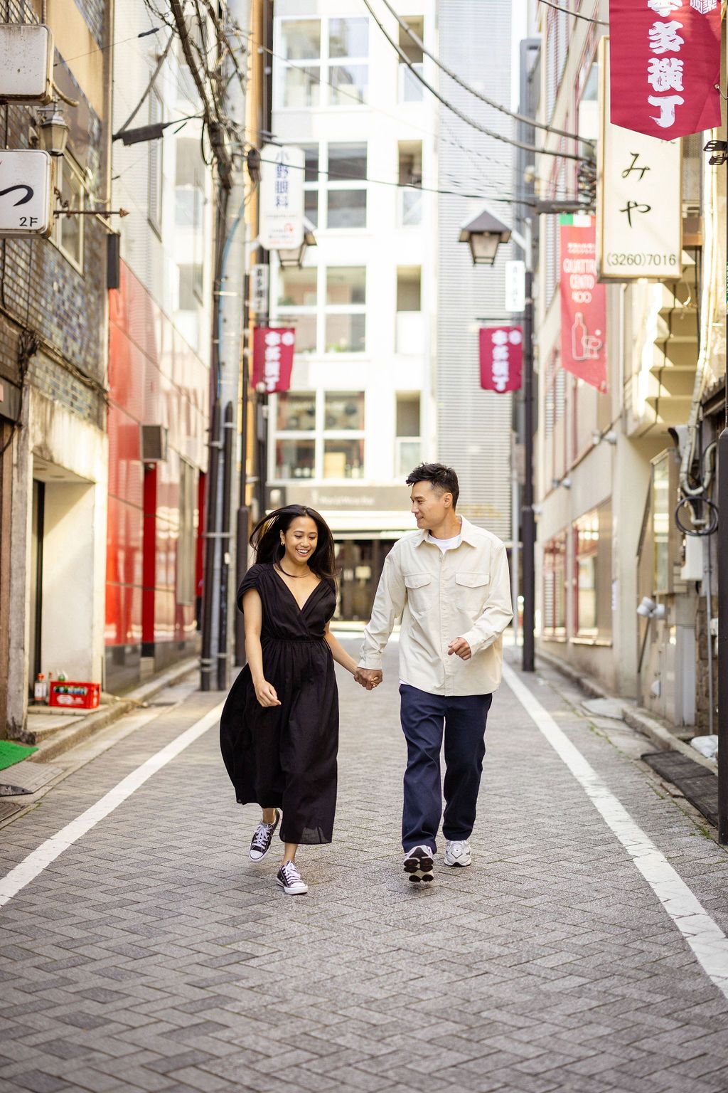 A couple strolling hand in hand through a charming Japanese alley with red banners.