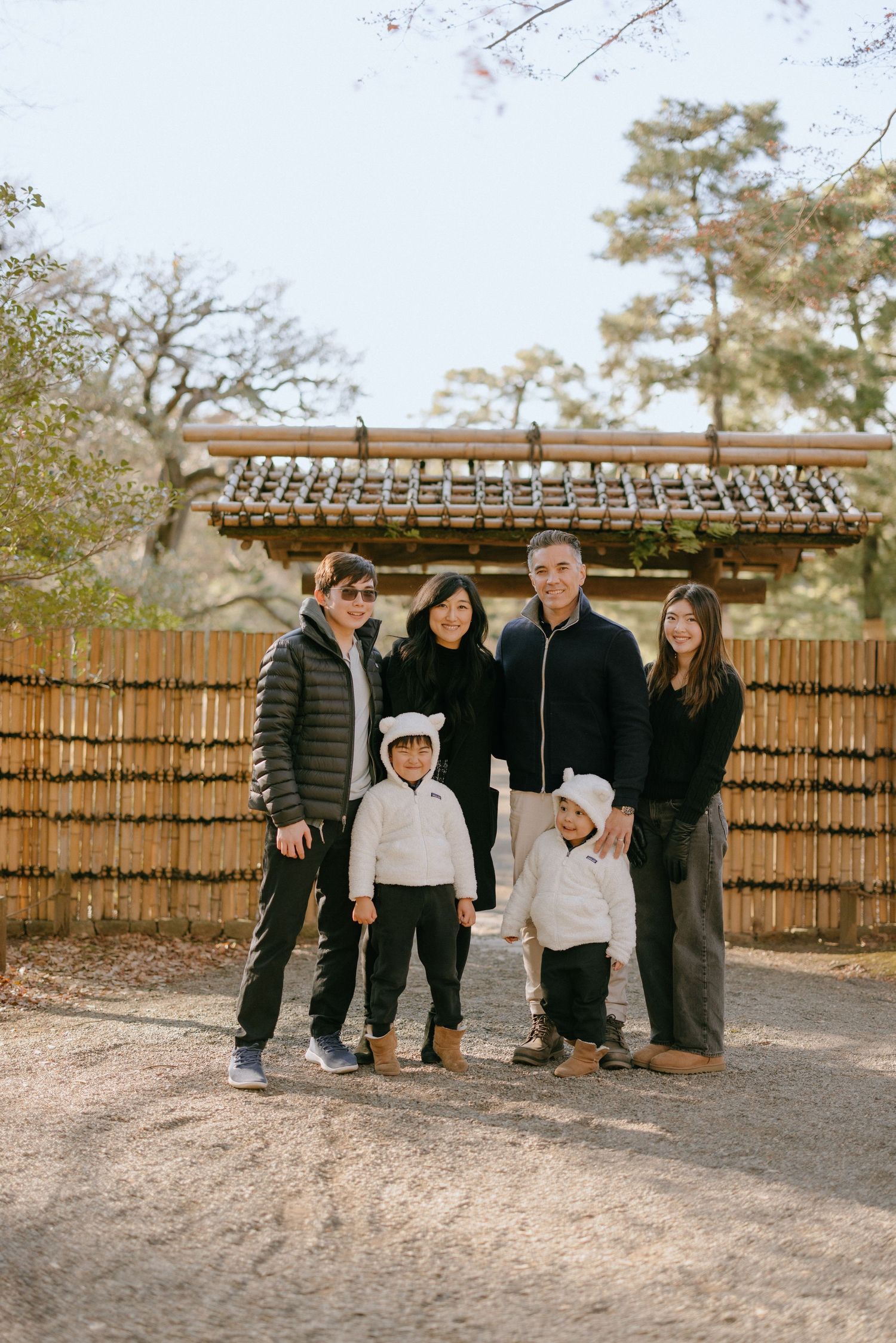 A group stands in front of a traditional bamboo fence and Japanese-style building on a sunny autumn day.