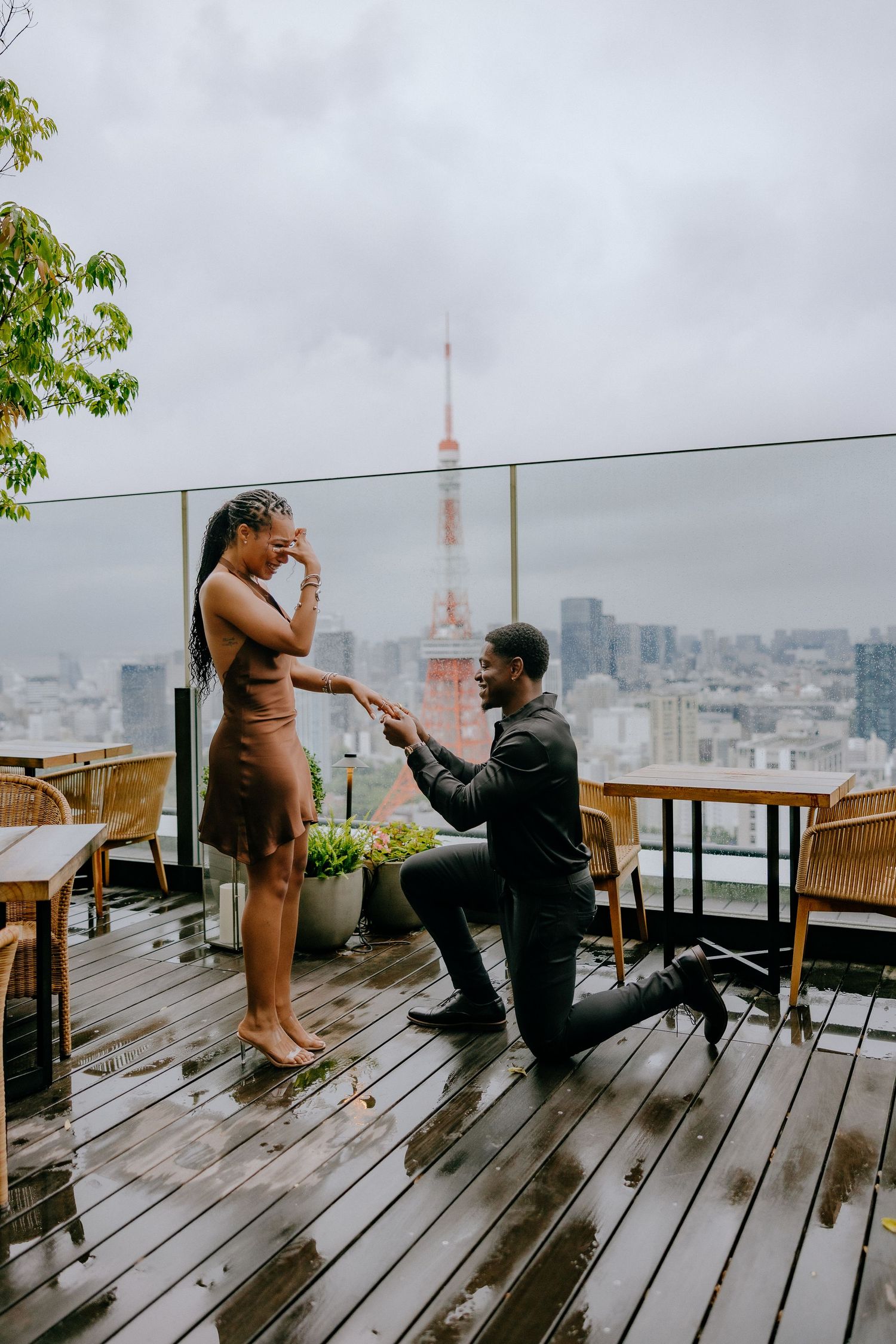 A couple shares a special moment during a rooftop proposal with the city skyline in the background.