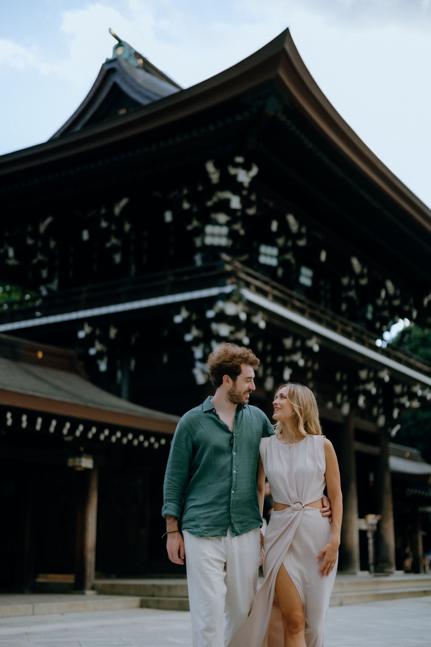 A couple stands together in front of traditional Japanese temple Meiji Shrine for their engagement photoshoot