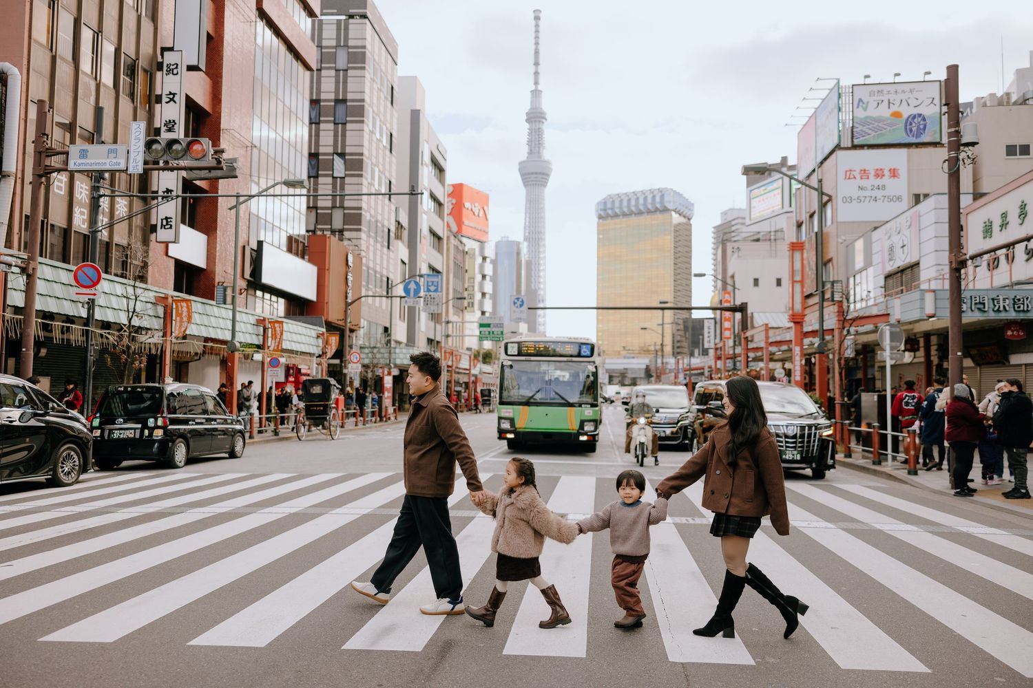 People crossing a busy intersection in Tokyo with the iconic Skytree tower visible in the background.