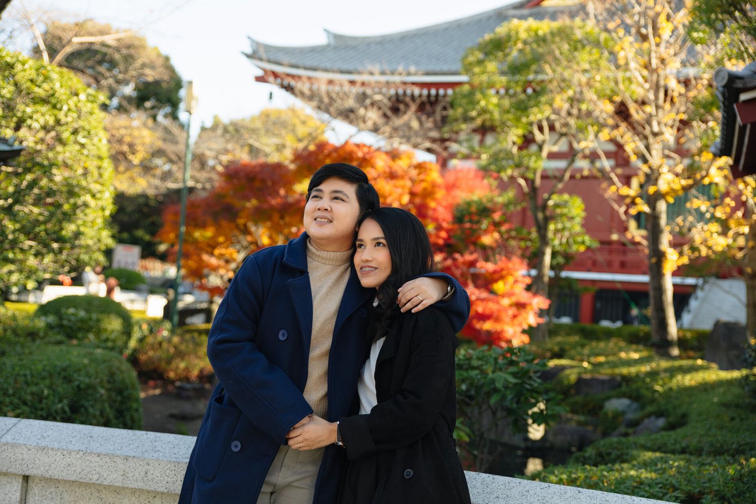 Couple enjoying autumn scenery at Japanese garden with temple in background.