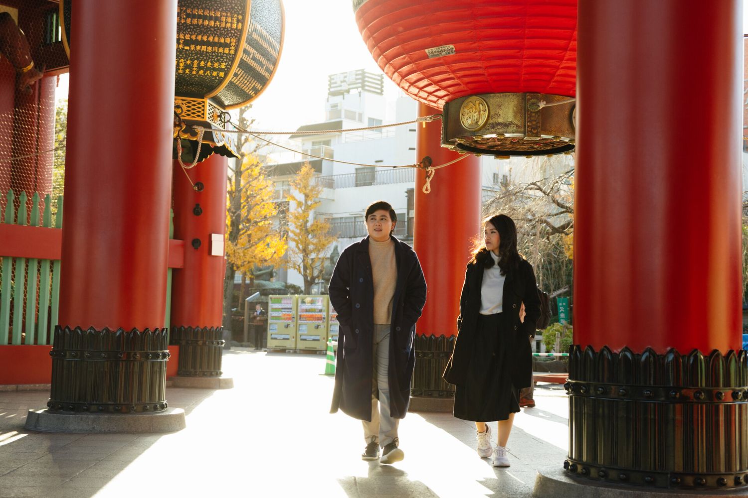 Couple walking through traditional Japanese temple gate with red lanterns.
