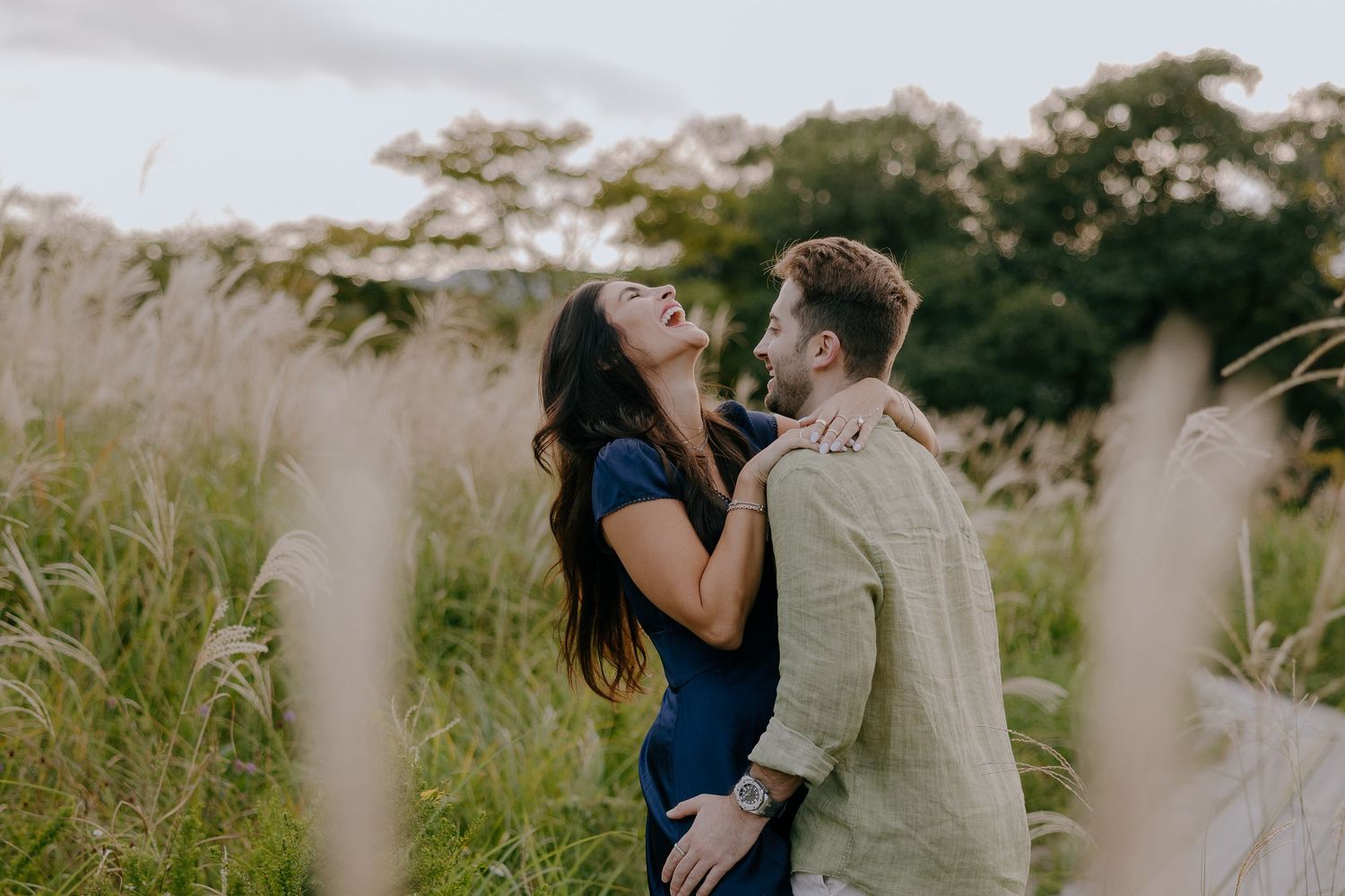 A couple embraces in a golden field during sunset while surrounded by tall grass and natural light at Hakone Botanical gardens