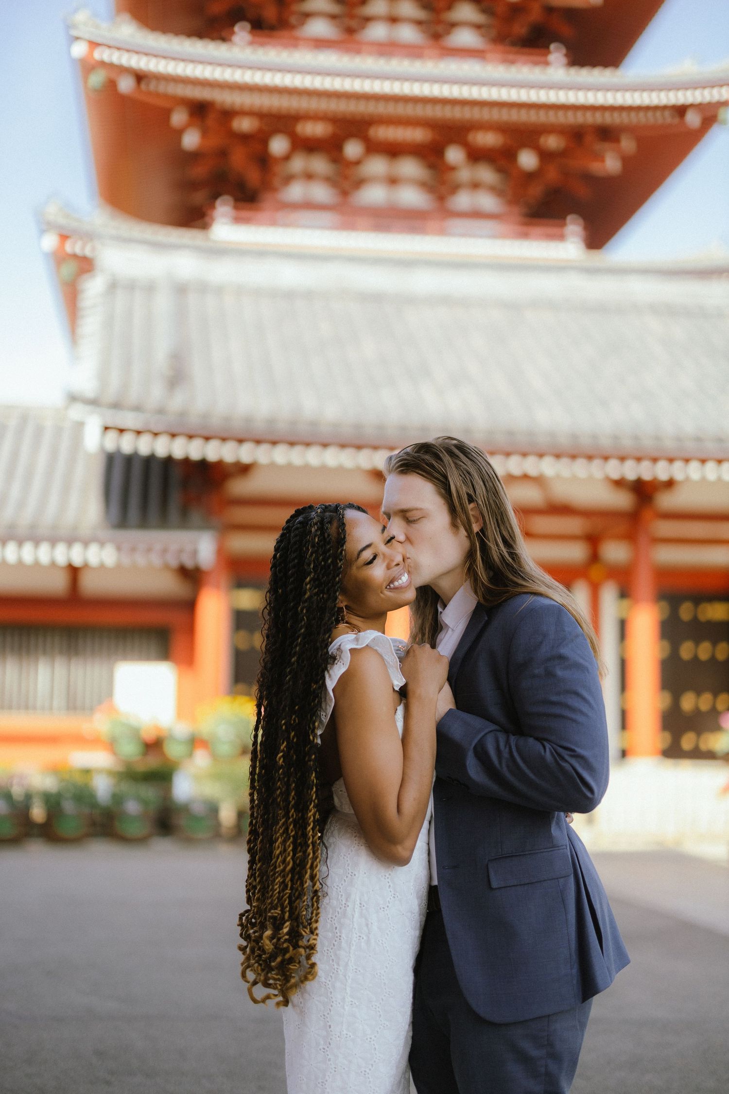 Intimate moment between couple at Japanese shrine with traditional orange pagoda architecture.