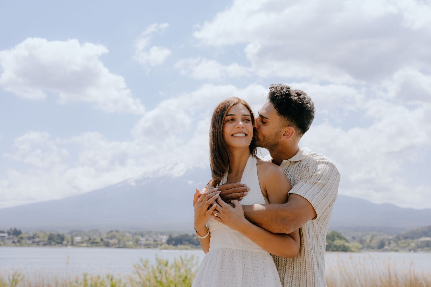 A romantic couple sharing an intimate moment outdoors with mountains and a lake in the background.