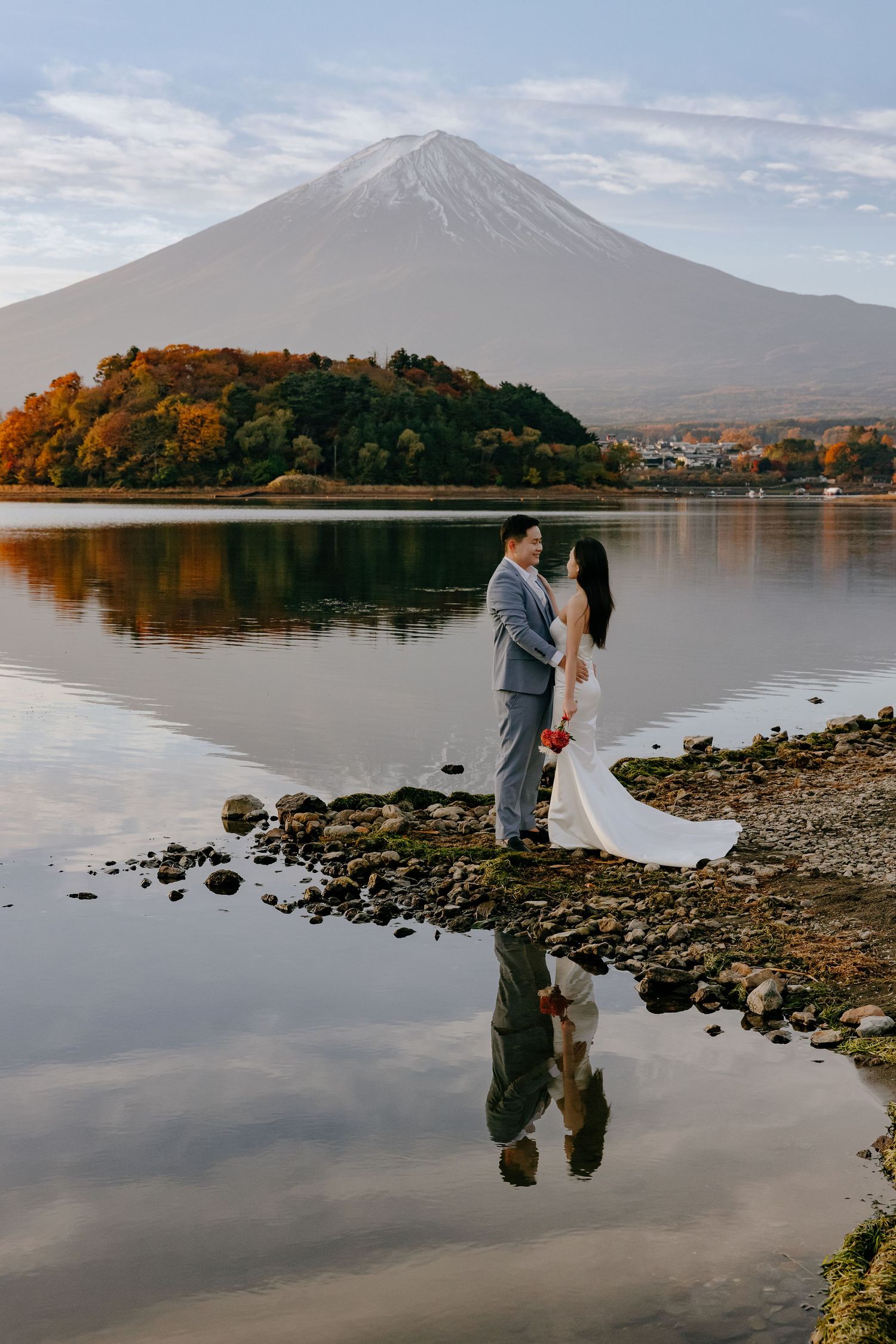 A couple stands by Lake Kawaguchiko with Mount Fuji rising majestically in the background during autumn.