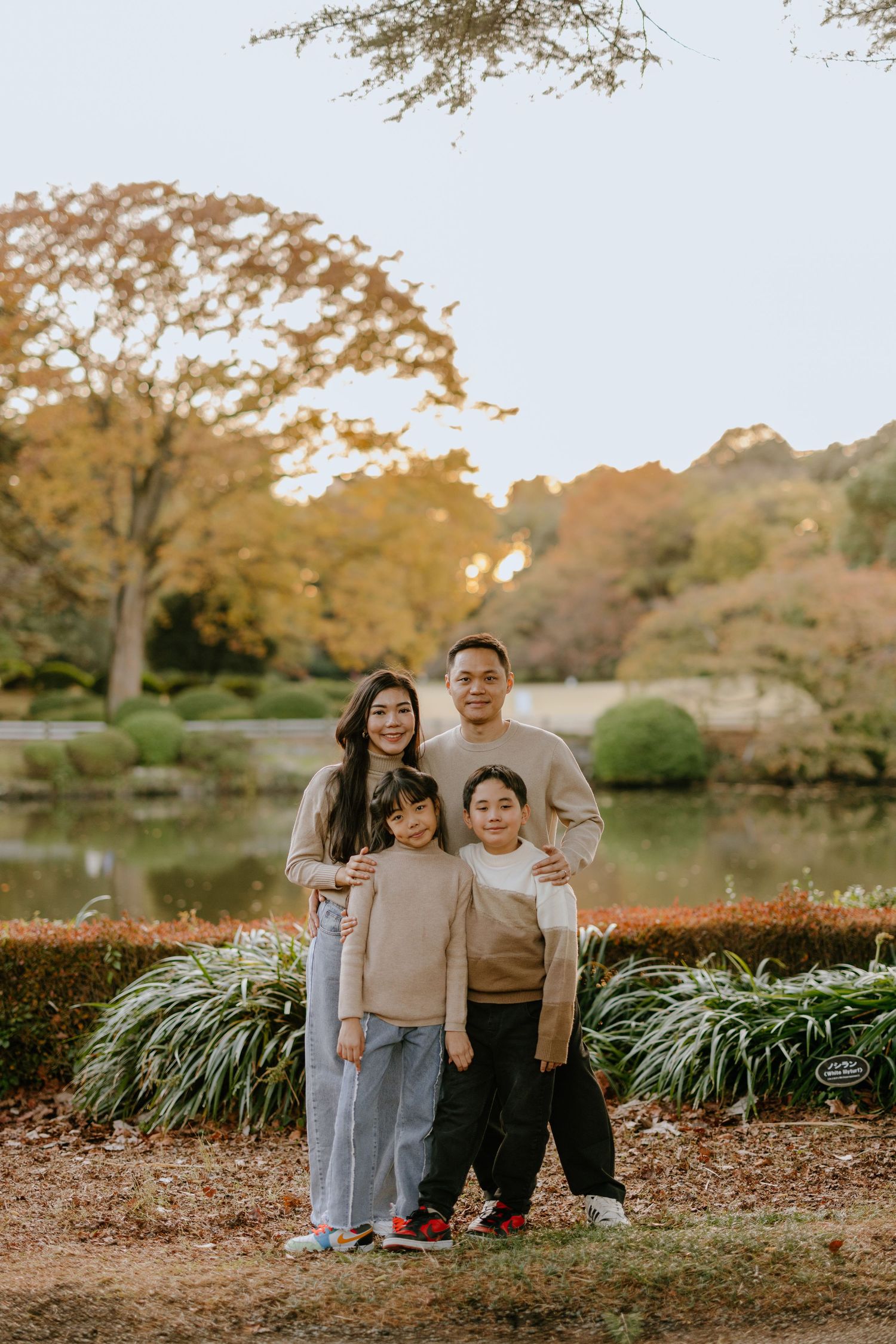 A family poses together on an autumn day in a park with golden trees and ornamental grasses in the background.