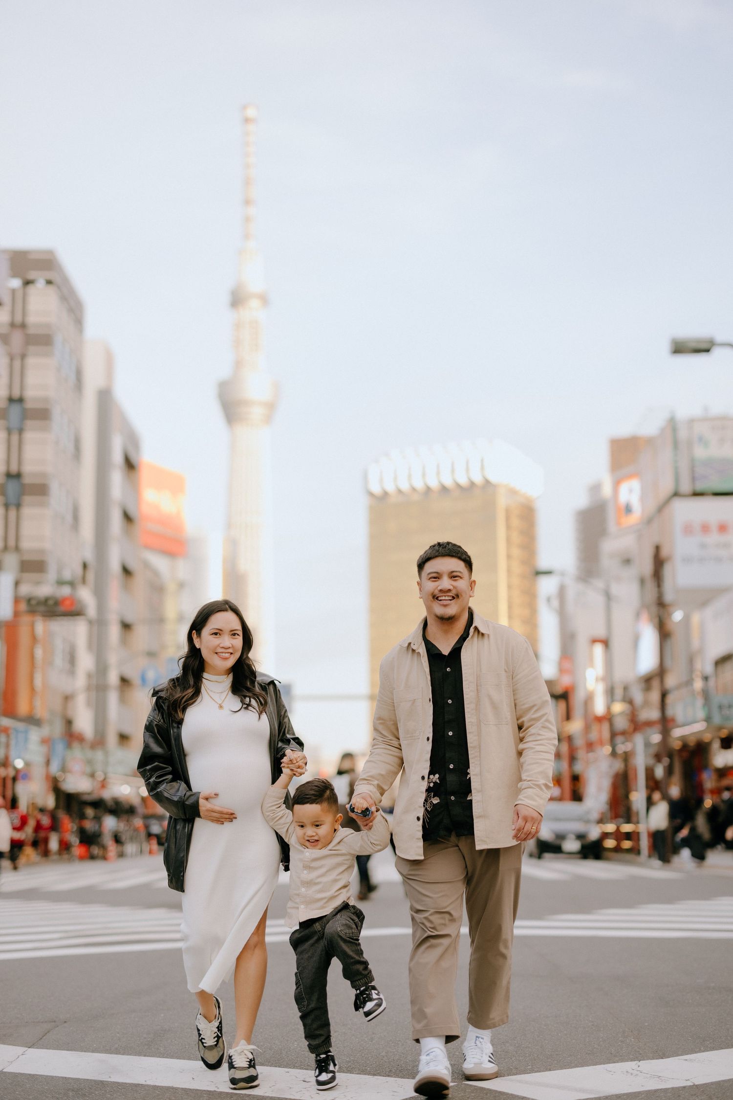 A family walks together on a city street in Tokyo with the distinctive Tokyo Skytree visible in the background.