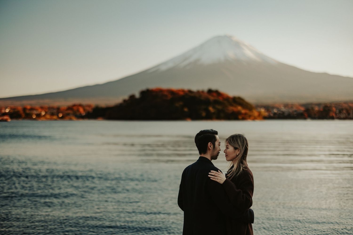 A couple embraces against the backdrop of Mount Fuji and Lake Kawaguchiko at sunset.