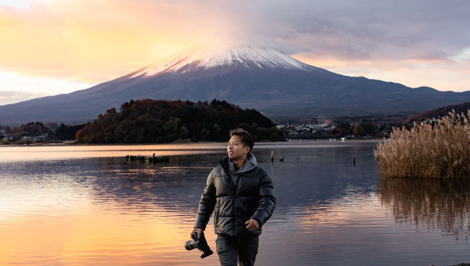 Photographer standing by a serene lake with iconic snow-capped Mount Fuji at sunset in Japan.