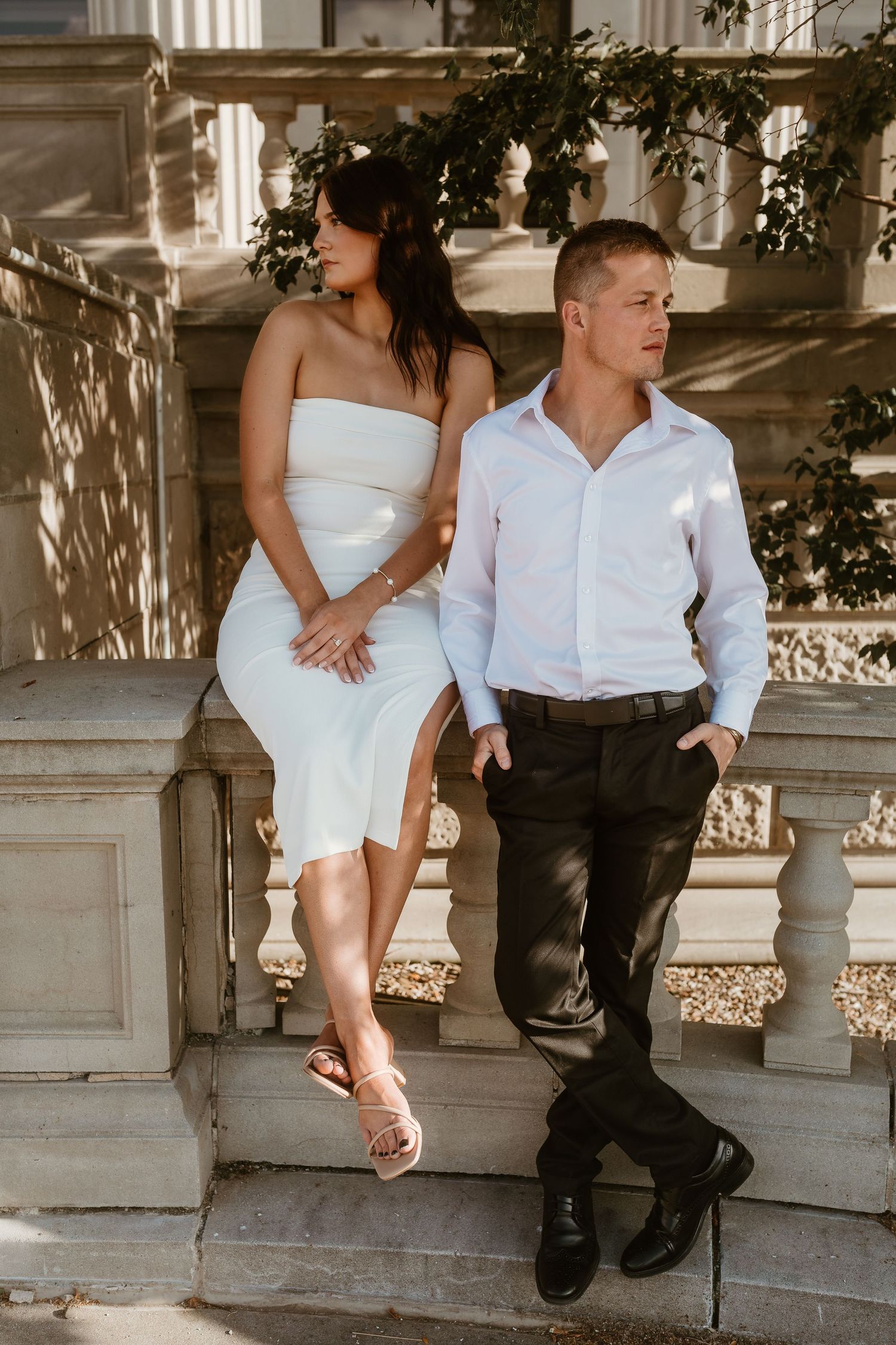 Casual portrait of couple in white attire lounging on ornate stone steps.