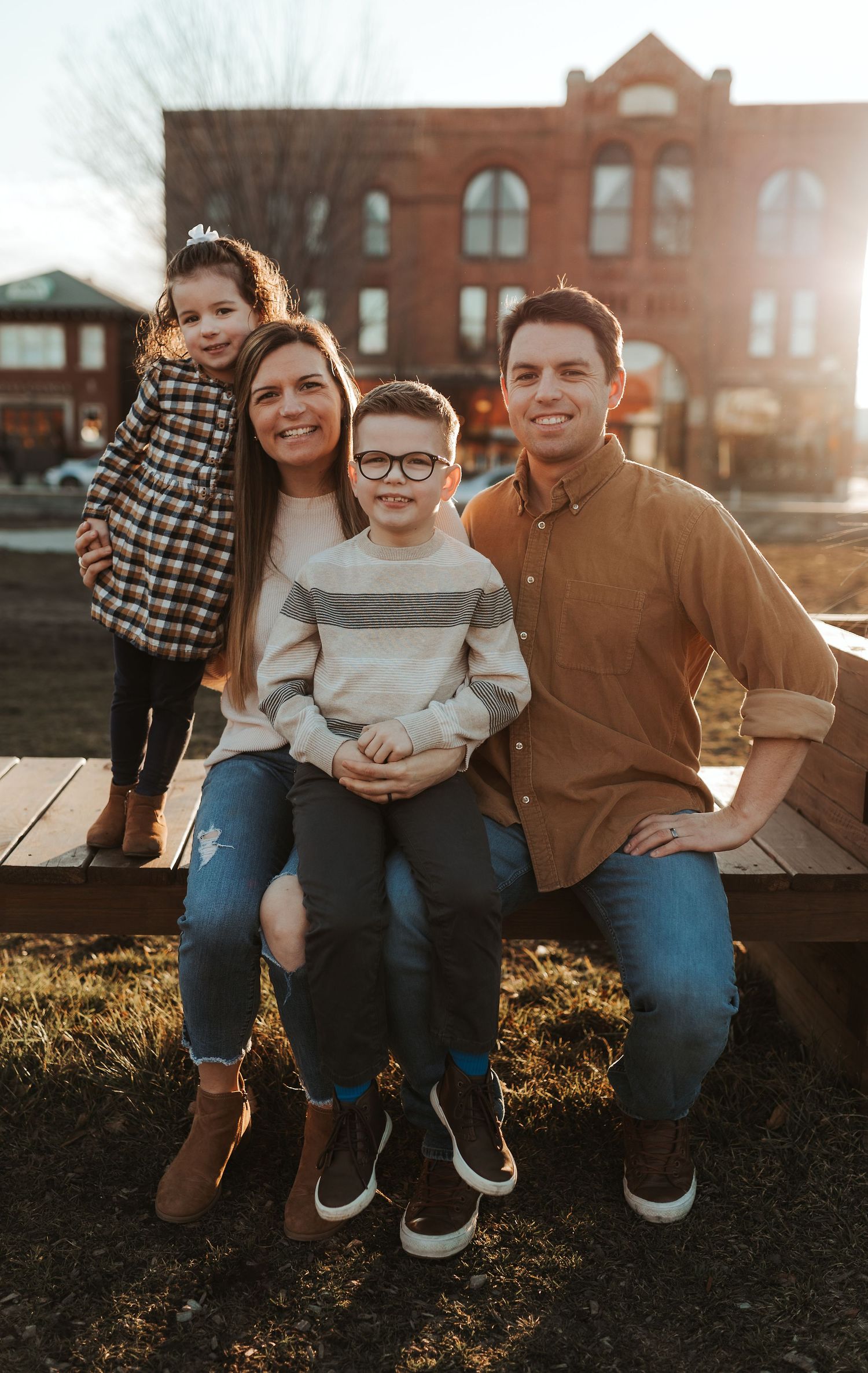 A sunlit family portrait taken outdoors against a vintage brick building backdrop.