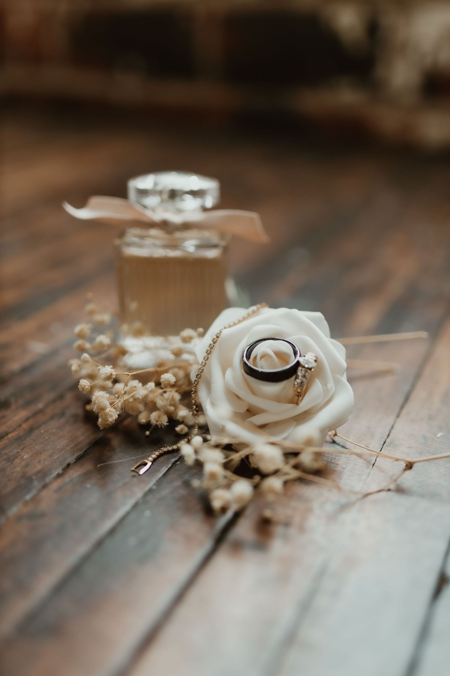 Wedding rings displayed on wooden surface with white rose and baby's breath florals.