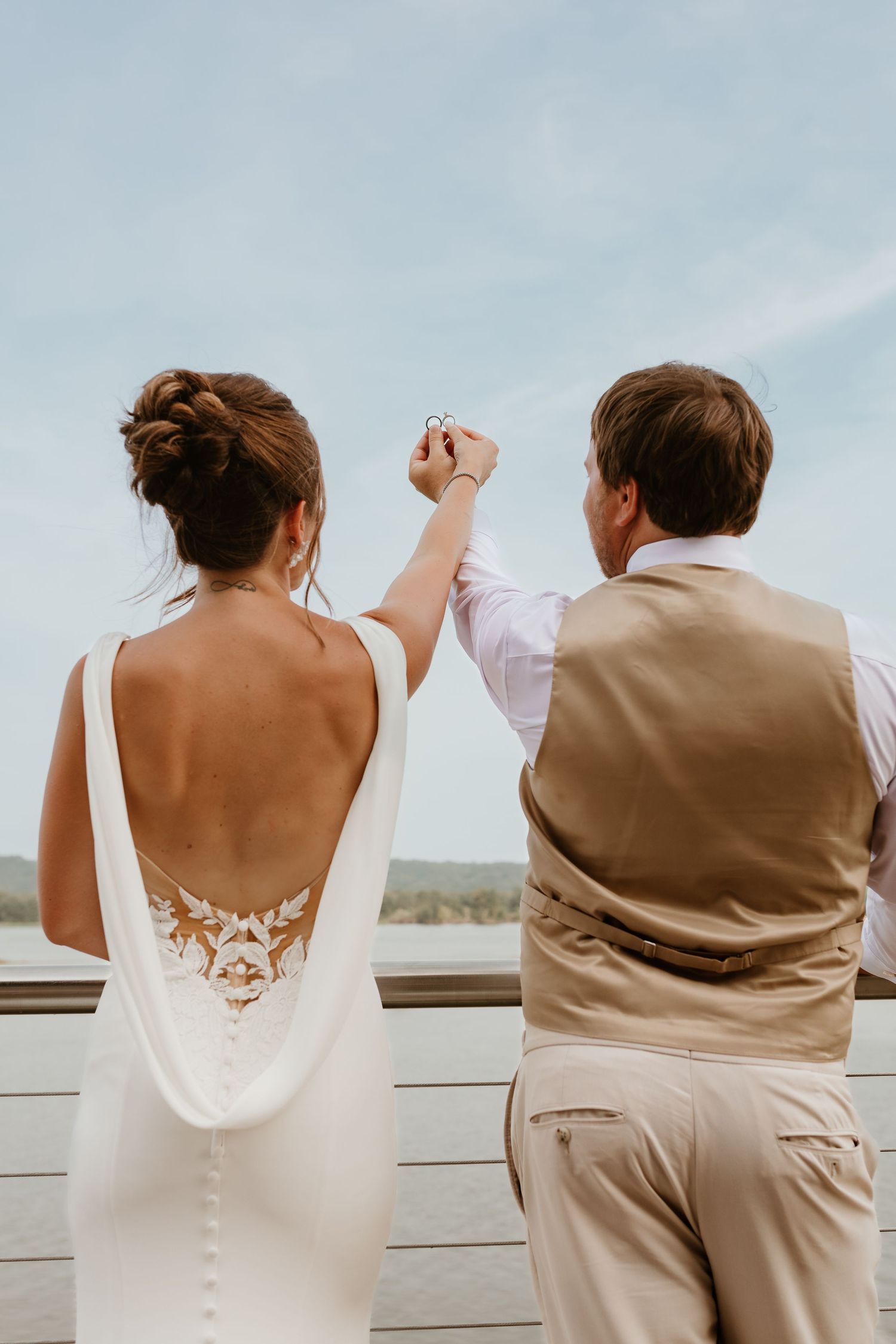 Newlyweds raise joined hands in celebration while looking out over scenic view.