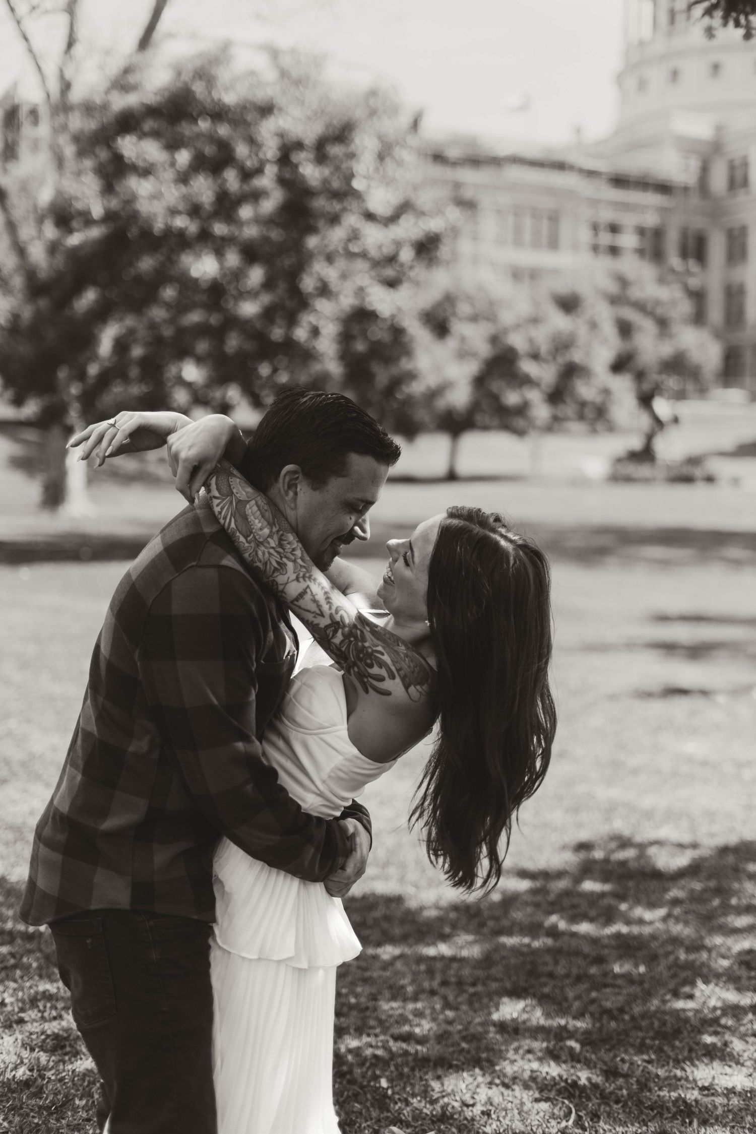 A romantic black and white photograph shows a couple embracing in a park, with trees and buildings in the background.