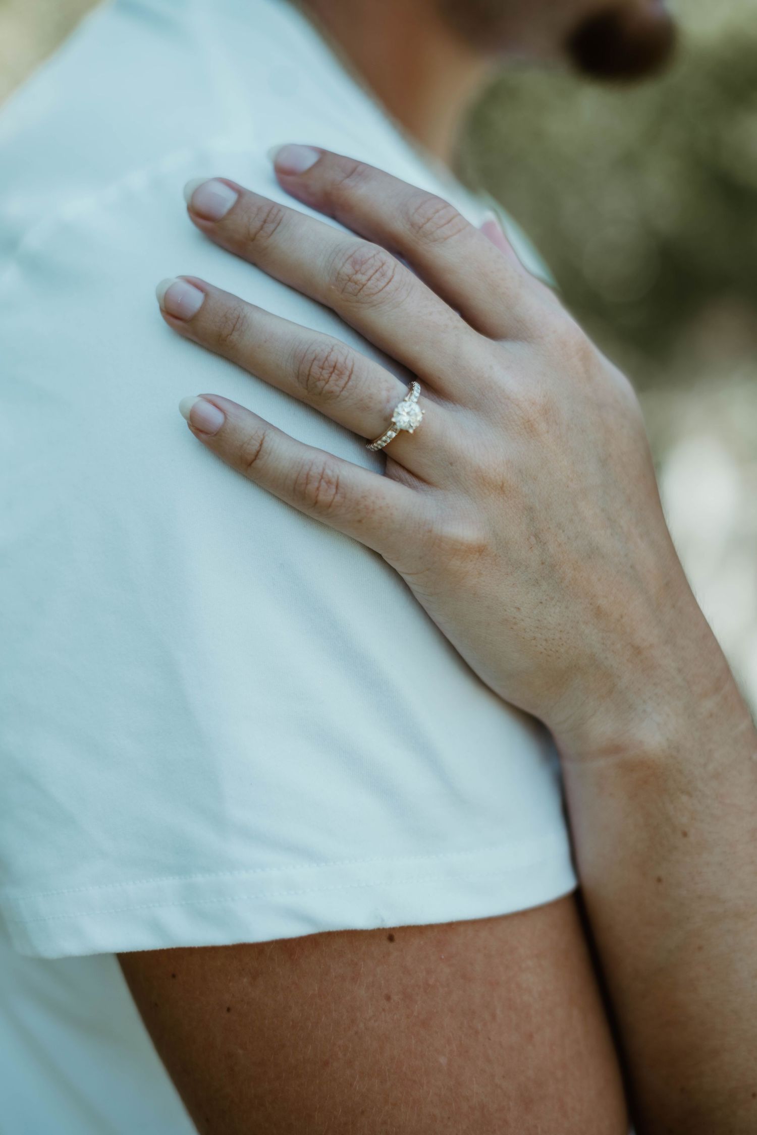 Close-up view of a hand resting on a white shirt sleeve showing an elegant diamond engagement ring.