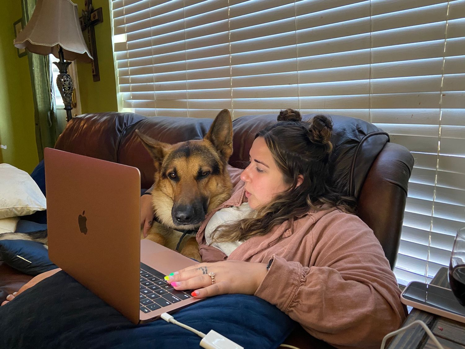 A collie dog rests its head on someone's lap while they work on a laptop computer.