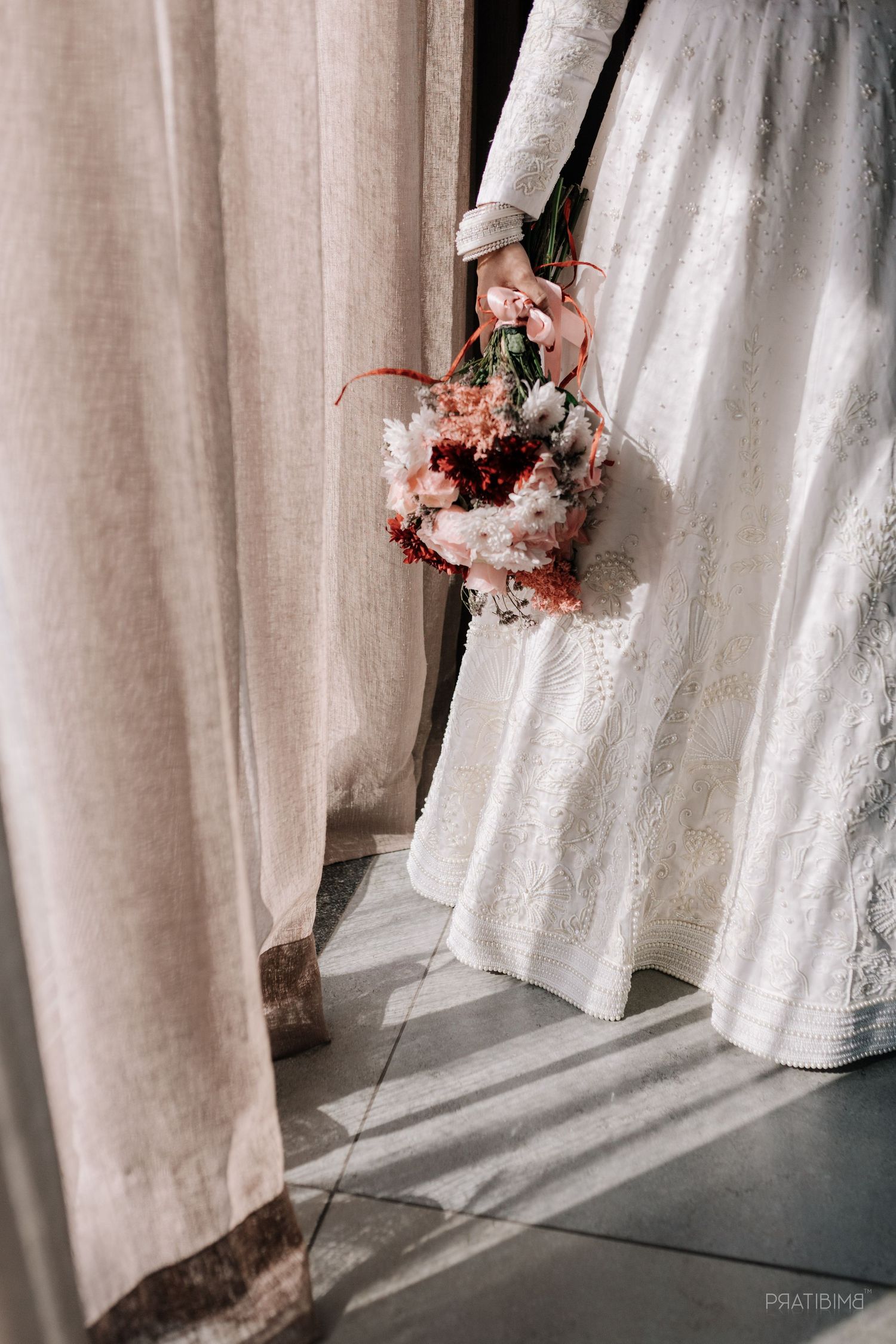 A delicate bouquet of pink flowers held against soft curtains in natural light.